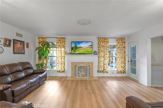 living room featuring a fireplace with flush hearth, wood finished floors, and visible vents