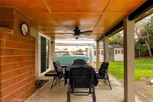 view of patio featuring a storage shed, outdoor dining area, a ceiling fan, and an outdoor structure