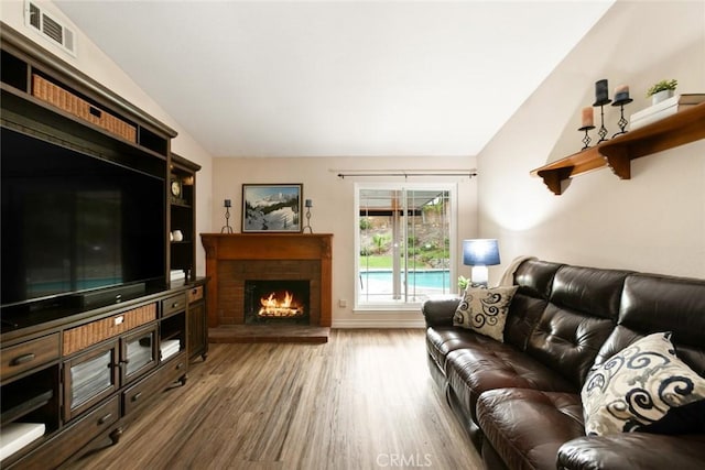 living room featuring lofted ceiling, a brick fireplace, wood finished floors, and visible vents