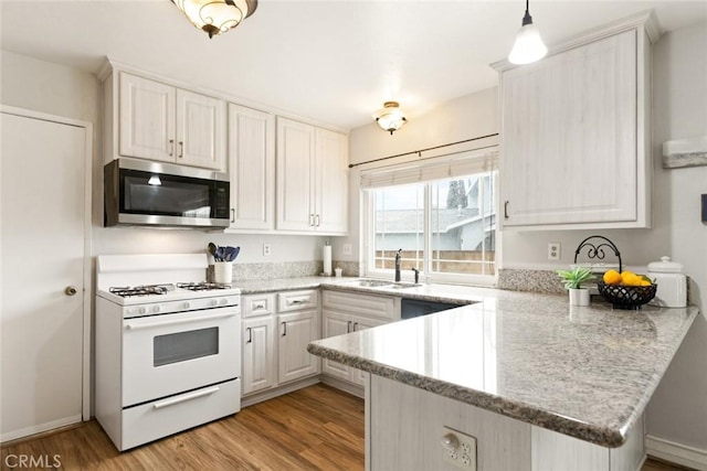 kitchen with light wood-style flooring, stainless steel microwave, a peninsula, a sink, and gas range gas stove