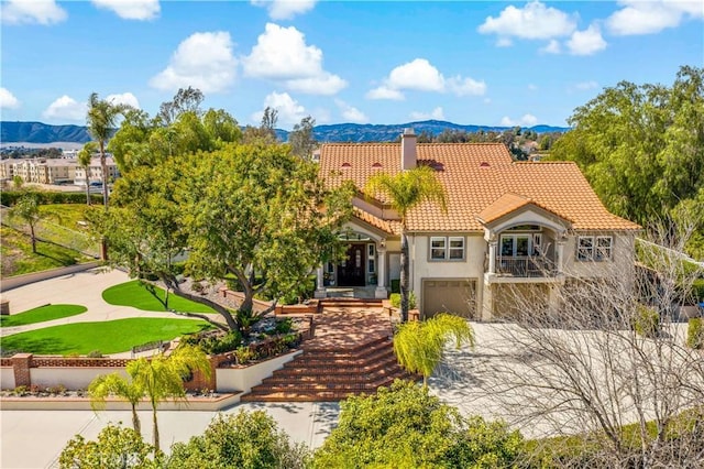 mediterranean / spanish-style home featuring a tiled roof, stucco siding, a chimney, a garage, and a mountain view