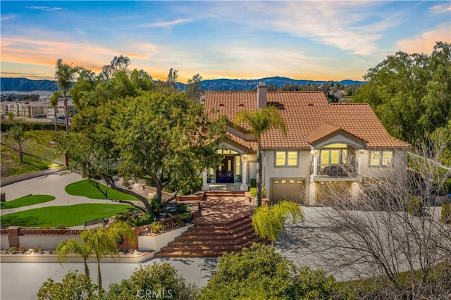 mediterranean / spanish house featuring a tile roof, stucco siding, a chimney, a garage, and a mountain view