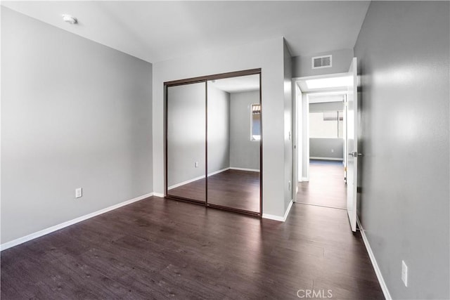 unfurnished bedroom with visible vents, baseboards, a closet, and wood finished floors