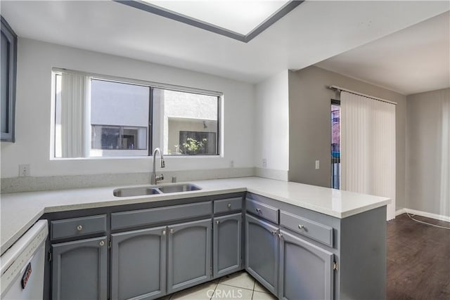 kitchen featuring light countertops, gray cabinets, a peninsula, white dishwasher, and a sink