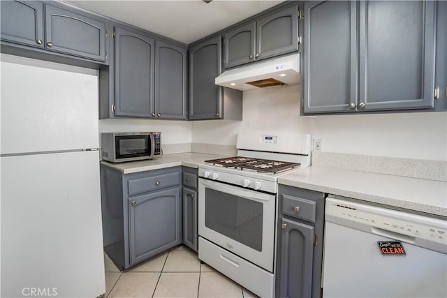 kitchen with under cabinet range hood, white appliances, light countertops, and light tile patterned floors