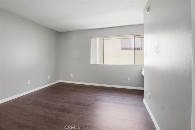 spare room featuring baseboards and dark wood-style floors