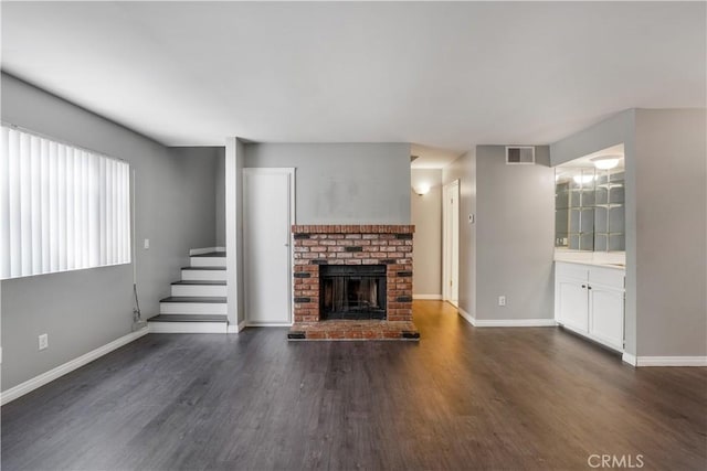 unfurnished living room with dark wood-style floors, visible vents, and baseboards