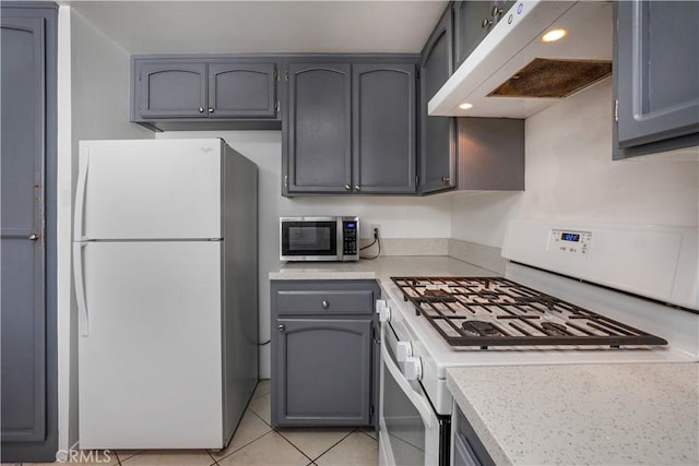 kitchen featuring white appliances, light tile patterned floors, gray cabinets, light countertops, and under cabinet range hood