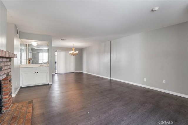 unfurnished living room featuring dark wood finished floors, a notable chandelier, a brick fireplace, and a sink