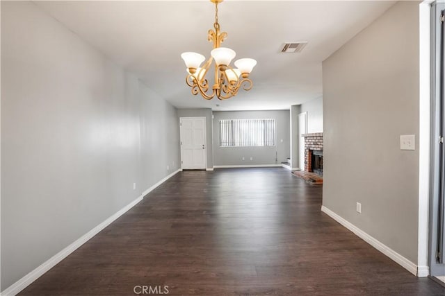 unfurnished living room featuring visible vents, baseboards, a brick fireplace, a chandelier, and dark wood-style flooring