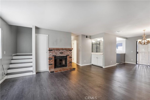 unfurnished living room featuring baseboards, a notable chandelier, a brick fireplace, and dark wood-style flooring