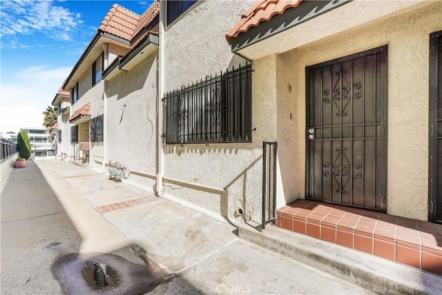 doorway to property featuring a tiled roof, fence, and stucco siding