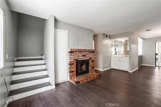 unfurnished living room featuring stairway, visible vents, a sink, dark wood-type flooring, and a brick fireplace