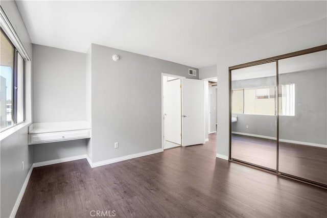 unfurnished bedroom featuring multiple windows, wood finished floors, visible vents, and baseboards