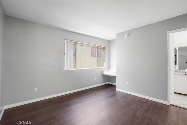 unfurnished bedroom featuring wood finished floors, built in desk, ensuite bathroom, and baseboards