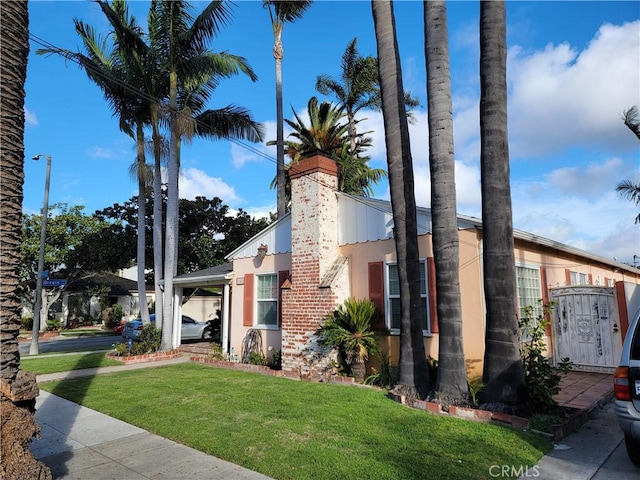 view of side of property with stucco siding, a chimney, and a yard