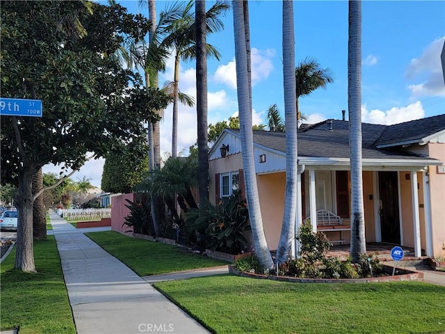 view of side of property featuring a shingled roof, covered porch, a lawn, and stucco siding