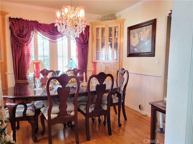 dining space featuring light wood-style floors, wainscoting, ornamental molding, and an inviting chandelier