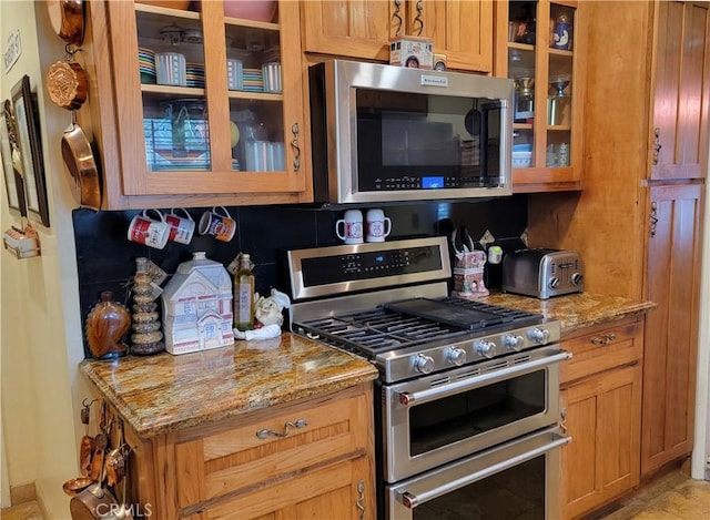 kitchen featuring appliances with stainless steel finishes, glass insert cabinets, and light stone countertops