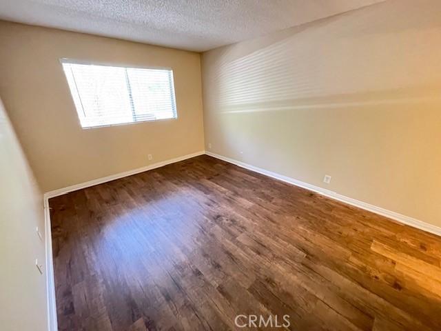 empty room with dark wood-style floors, a textured ceiling, and baseboards