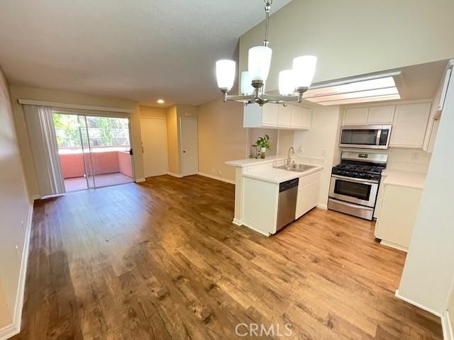 kitchen with appliances with stainless steel finishes, a peninsula, light countertops, light wood-style floors, and a sink