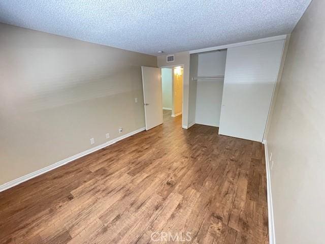 unfurnished bedroom with a textured ceiling, a closet, wood finished floors, and baseboards