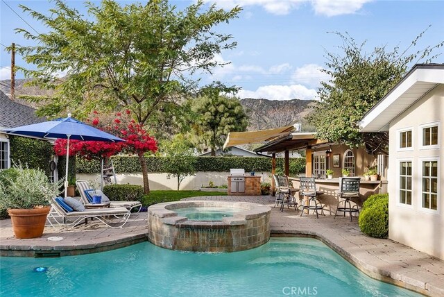 view of swimming pool featuring a patio, an outdoor kitchen, outdoor wet bar, an in ground hot tub, and a fenced in pool