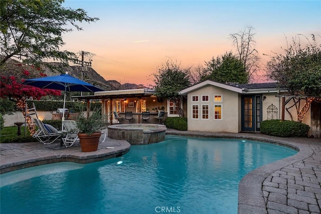 pool at dusk with a patio area and a pool with connected hot tub