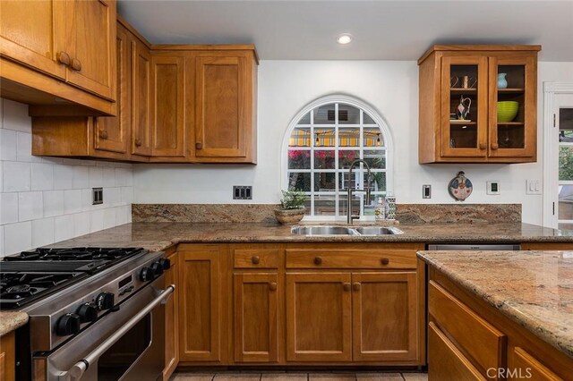 kitchen featuring brown cabinets, stone countertops, high end range, and a sink