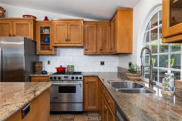 kitchen featuring a sink, vaulted ceiling, appliances with stainless steel finishes, backsplash, and brown cabinets