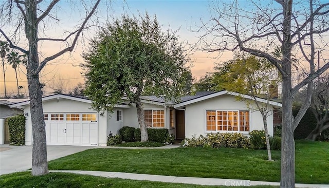 ranch-style house with a garage, driveway, a lawn, and stucco siding