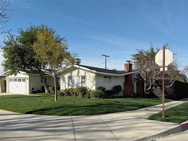 ranch-style house with an attached garage, a chimney, a front lawn, and stucco siding