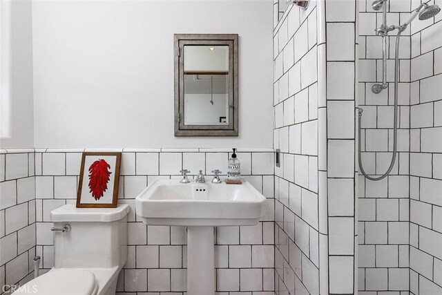 bathroom with toilet, a sink, a tile shower, and tile walls