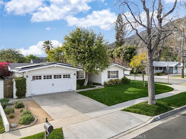 ranch-style house with stucco siding, solar panels, an attached garage, a front yard, and driveway