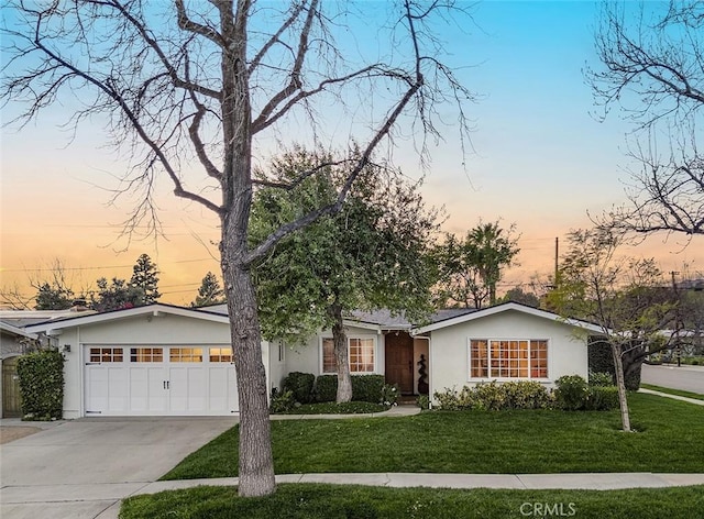 ranch-style home with a lawn, driveway, an attached garage, and stucco siding