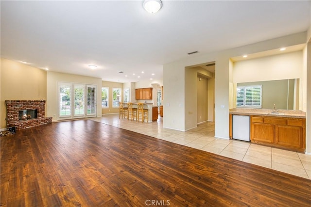 unfurnished living room with a fireplace, a sink, visible vents, and light wood-style floors