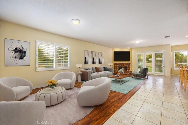 living area with a brick fireplace, light tile patterned flooring, visible vents, and baseboards