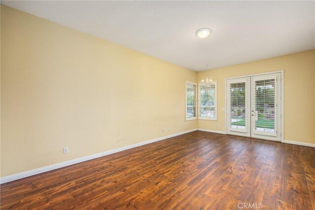 unfurnished room featuring an inviting chandelier, baseboards, and dark wood-style flooring