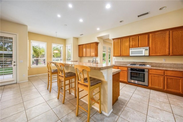 kitchen featuring white appliances, visible vents, a breakfast bar area, brown cabinets, and light tile patterned flooring