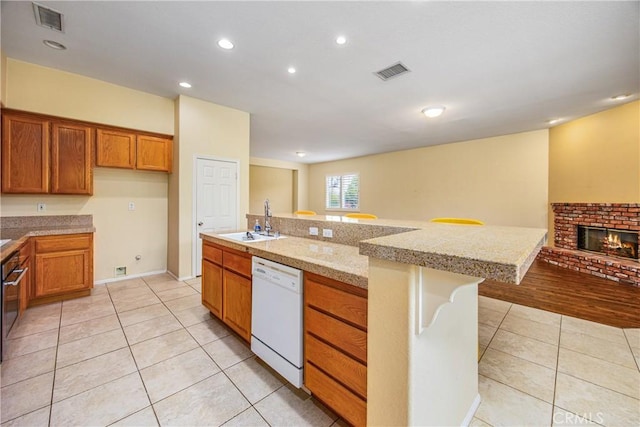 kitchen featuring visible vents, brown cabinetry, light tile patterned flooring, a sink, and dishwasher