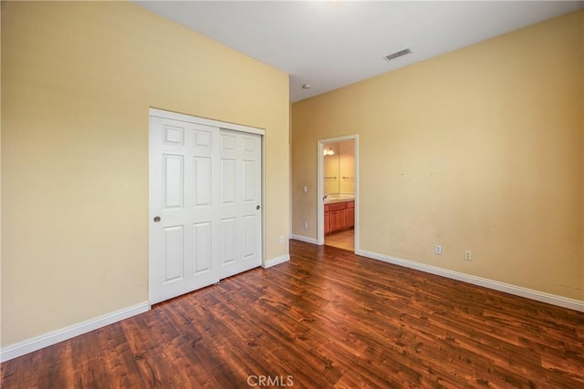 unfurnished bedroom featuring dark wood-style flooring, a closet, visible vents, and baseboards