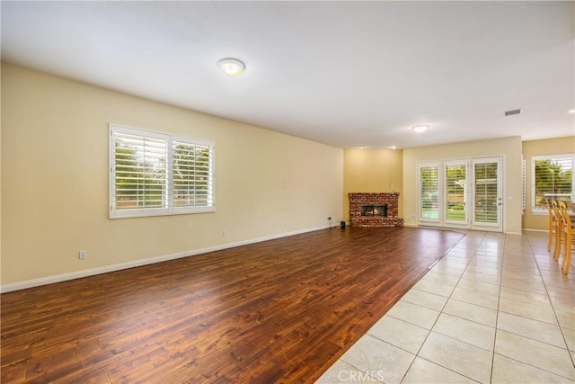 unfurnished living room with light wood-type flooring, visible vents, a fireplace, and baseboards