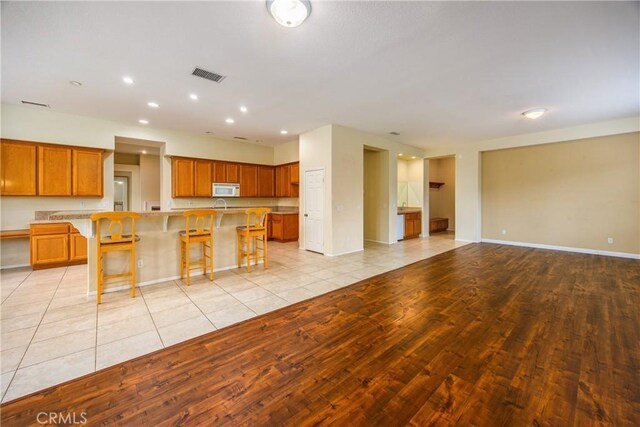 kitchen with visible vents, brown cabinetry, white microwave, open floor plan, and a kitchen breakfast bar