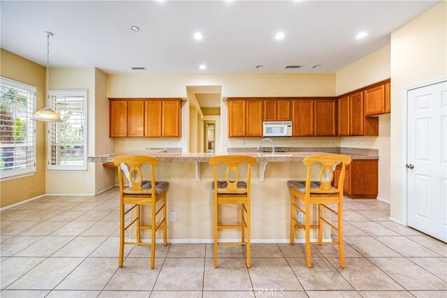 kitchen with white microwave, light tile patterned floors, visible vents, and brown cabinetry