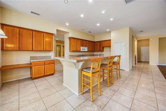 kitchen with light tile patterned floors, white microwave, brown cabinetry, and visible vents