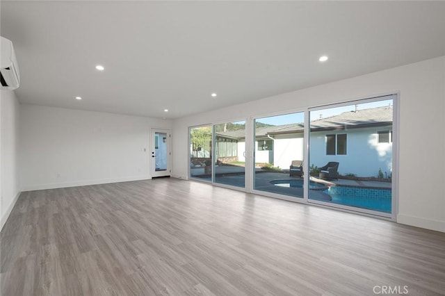 unfurnished living room with wood finished floors, baseboards, recessed lighting, and a wall unit AC