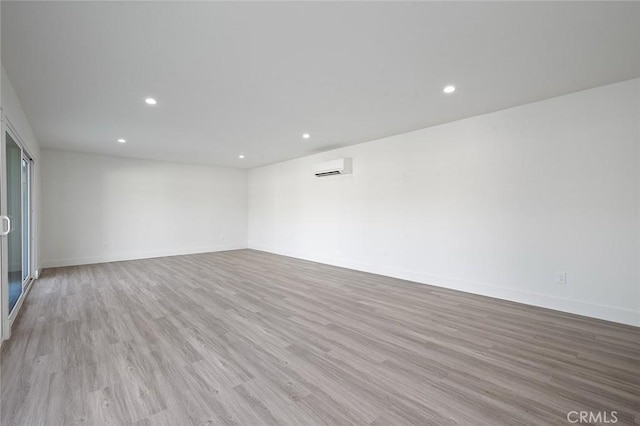 unfurnished room with recessed lighting, a wall unit AC, wood finished floors, and baseboards