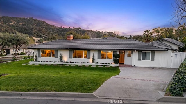 ranch-style home with a chimney, driveway, a front yard, and a tiled roof