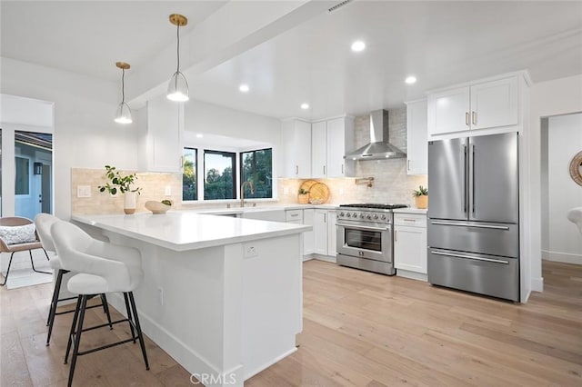 kitchen featuring high quality appliances, wall chimney range hood, a peninsula, light wood-style flooring, and recessed lighting