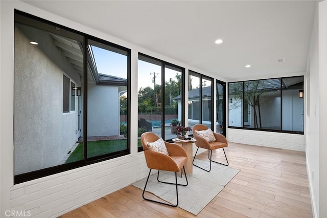 sunroom with wood finished floors, a wall of windows, and recessed lighting